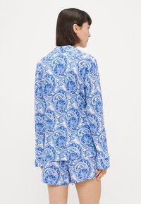 Blue and white paisley patterned pajama set featuring a long-sleeve button-up shirt and matching shorts, made from lightweight fabric.