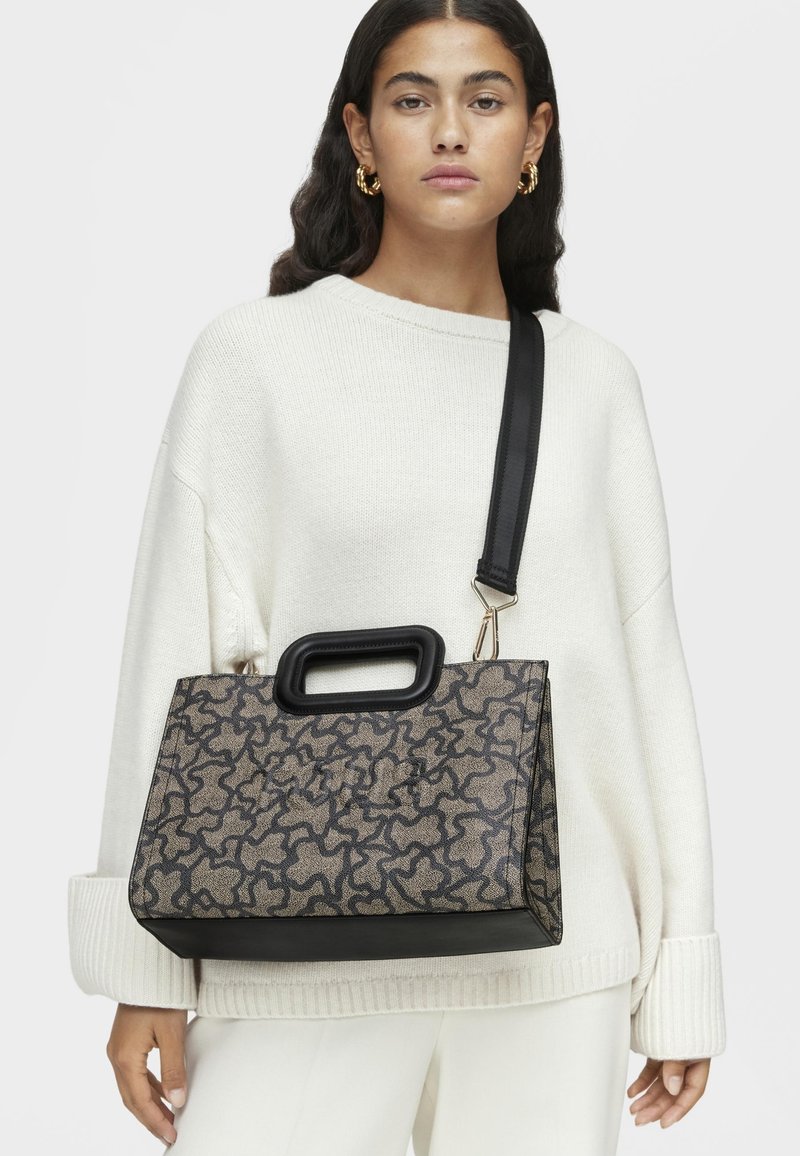 Teksturowana torebka w czerni i złocie z geometrycznym wzorem, o wyraźnej formie i górnym uchwycie. Dołączony regulowany czarny pasek.