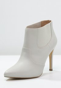 Witte leren enkelboot met een spitse neus, elastische zijpanelen en dunne hak. Soepele textuur met minimale ontwerpdetails.