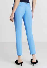 Pantaloni su misura di colore azzurro chiaro con una vestibilità slim e una texture liscia. Presentano tasche posteriori e una lunghezza cropped, abbinati a mule nere con tacco.