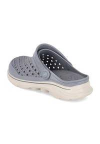 Gray slip-on shoe made of flexible material with a textured upper and cut-out design. Features a cream-colored sole and adjustable strap.