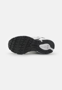 Semelle de chaussure de sport en noir et blanc avec caoutchouc texturé, présentant de profonds motifs de semelle et un logo New Balance. Transition lisse vers un bord blanc.