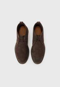 Brown suede ankle boots with a round toe, stitching detail, and a small pull tab at the heel. Leather insole and minimalist design.