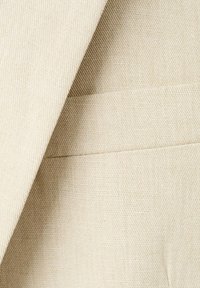 Tissu beige à tissage serré montrant un coin plié et une couture horizontale, mettant en valeur la texture et les détails des points.