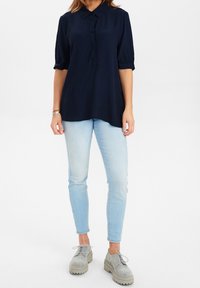 Blusa blu navy con bottoni e maniche corte, abbinata a jeans aderenti azzurri e scarpe con plateau grigie. La blusa presenta un colletto e una vestibilità comoda.