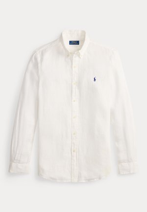 Camisa branca de linho, com botões e mangas longas, apresentando um colarinho clássico e um pequeno logotipo azul bordado no lado esquerdo do peito.