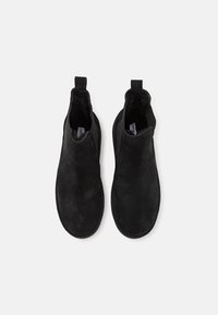 Černé semišové kotníkové boty s elastickými bočními panely, kulatou špičkou a poutky pro snadné obouvání. Hladká textura a minimalistický design.