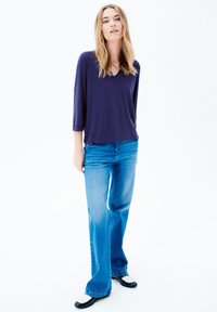 Paita navy lengan tiga per empat dipasangkan dengan jeans flared biru muda. Paita ini memiliki desain leher V, sementara jeansnya memiliki potongan klasik.