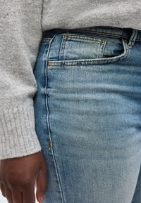 Άτομο που φοράει ανοικτό μπλε τζιν τζιν και ανοιχτό γκρι πλεκτό πουλόβερ με εμφανές χέρι στο πλάι.