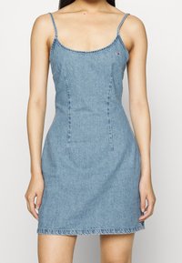 Jeansklänning med tunna axelband, en figurnära bodice och en utsvängd kjol. Ljusblå färg med fransat fåll och subtila sömnadsdetaljer.