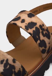 Nahaufnahme von Riemen in Braun- und Schwarztiermuster auf einer braunen Fußbett mit sichtbaren Nähten auf einer schwarzen Sohle.