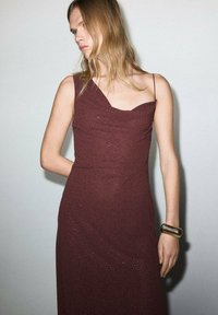 Burgundské šaty s jedným ramienkom, s textúrovanými detailmi a priliehavým strihom. Doplněné kovovým zlatým náramkom na zápästí.