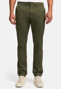 Chinos verde oliva con un diseño de pierna recta, hechos de un suave tejido de algodón, que cuentan con bolsillos frontales y un cierre de botón simple, llevados con zapatillas beige.