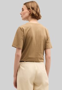 Camiseta de algodón marrón con mangas cortas, escote de crew y corte relajado, combinada con pantalones de color claro. Tejido suave y casual.