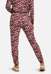 Bordo spalvos pižamos kelnės su žaismingu, pasikartojančiu ornamentų, lankų ir medžių raštu, turinčios elastinę juosmens juostą ir surinktus rankogalius.