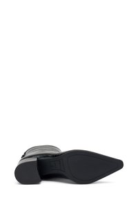 Bota de tobillo de cuero negro con puntera puntiaguda y tacón bajo. Textura suave con cremallera en el lateral y suela de goma texturizada.