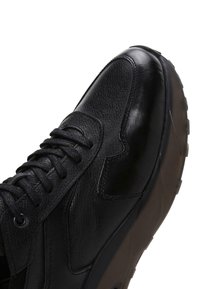 Sneakers en cuir noir avec tige texturée, design à lacets et semelle extérieure en caoutchouc contrastante. Présente des coutures discrètes et une silhouette élégante.