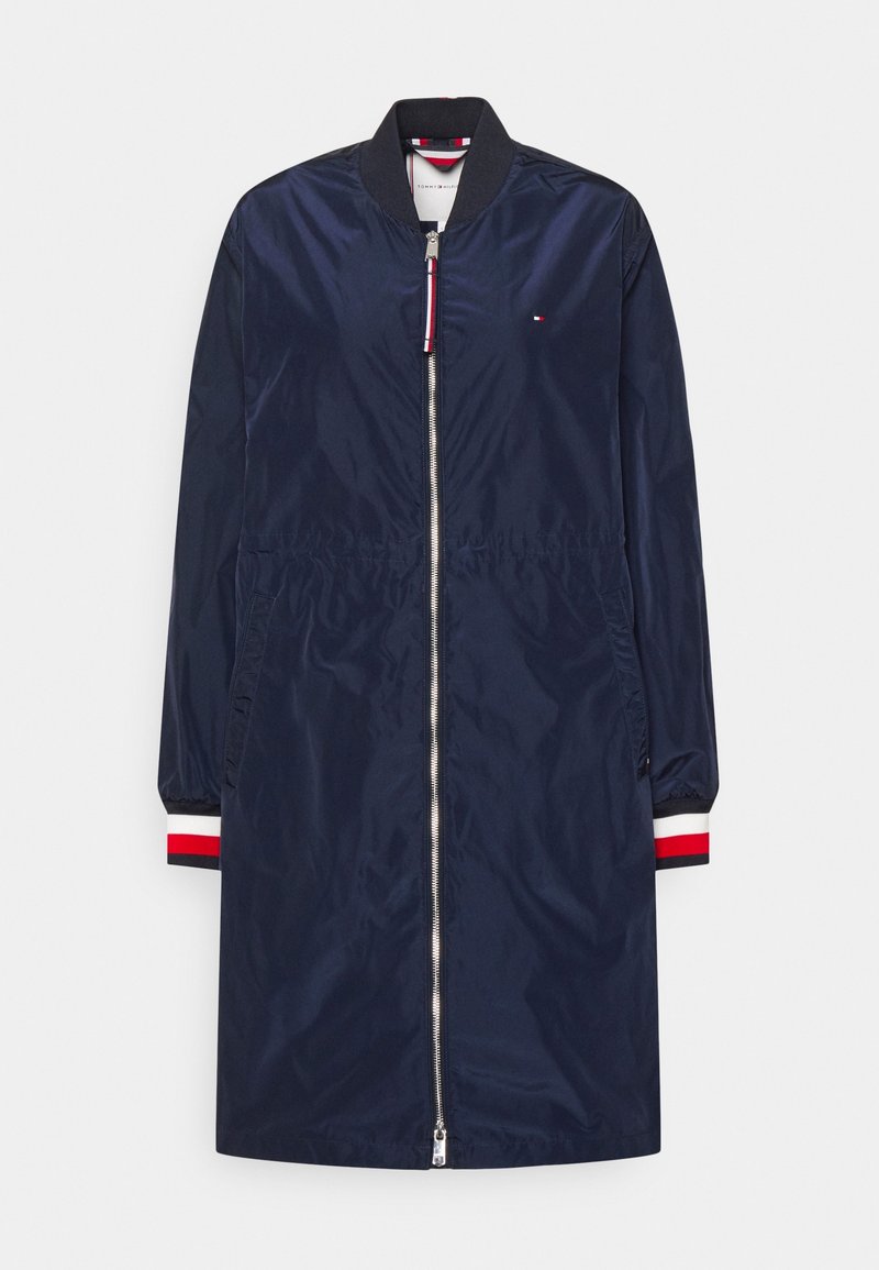 Veste bomber longue bleu marine avec fermeture éclair à l'avant, col et poignets côtelés avec rayures rouges, blanches et noires, et poches latérales.