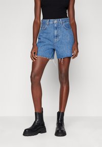 Pantalones cortos de mezclilla con cintura alta, dobladillo deshecho y un lavado de azul claro, combinados con botas de cuero negras hasta el tobillo. Textura suave y diseño casual.
