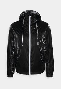 Svart lättviktsjacka med en glänsande yta, med huva, vit dragkedja och justerbara snoddar. Elastiska ärmslut och nederkant ingår.