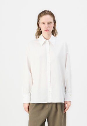 Camicia bianca con bottoni, realizzata in cotone, con colletto classico e maniche lunghe, caratterizzata da una vestibilità rilassata e una texture sottile.