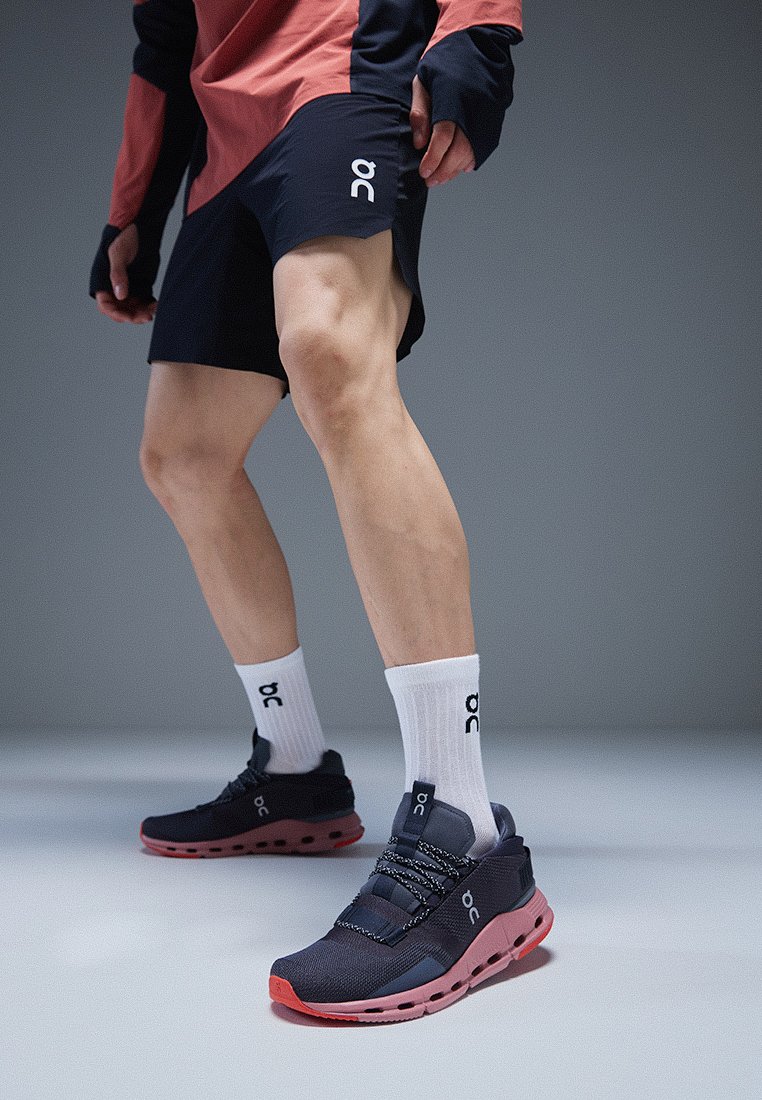 Zwarte en roze sportschoenen met een bovenwerk van mesh, reflecterende accenten en elastische veters, gecombineerd met witte sokken met logo en zwarte shorts.