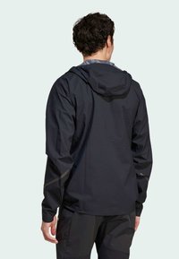 Čierna nepremokavá bunda s kapucňou, elastickými manžetami a reflexnými akcentmi. Ľahká tkanina s hladkou textúrou.