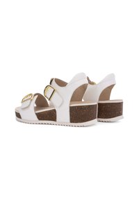 White platform sandals with two gold-buckled straps, cork-wrapped heel, and textured white sole. Smooth upper material with cutouts.