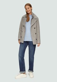 Grijze wollen peacoat met dubbele knopen, blauwe gebreide trui, donkere spijkerbroek en witte sneakers. Zachte textuur, casual pasvorm.