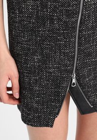 Robe texturée en noir et blanc avec une fermeture éclair latérale, agrémentée d'un bord noir contrastant près de l'ourlet et d'une silhouette ajustée.