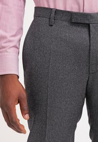 Graue Fischgrät-Hosen mit glatter Textur, flacher Vorderseite und Gürtelschlaufen, kombiniert mit einem rot-weiß gestreiften Langarmshirt.