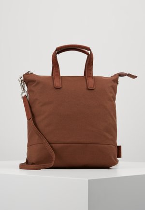 Sac en tissu marron de forme carrée avec deux poignées courtes en cuir et une bandoulière réglable, présenté sur un fond neutre.