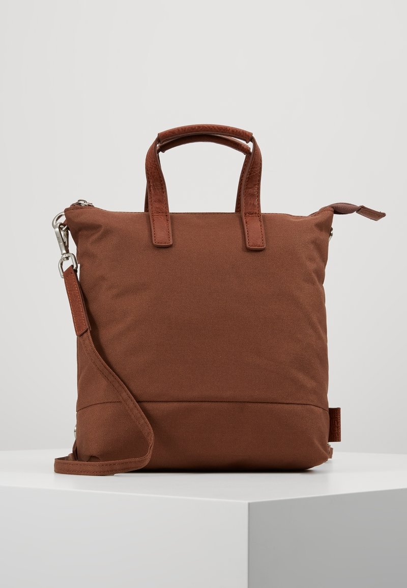 Sac en tissu marron de forme carrée avec deux poignées courtes en cuir et une bandoulière réglable, présenté sur un fond neutre.