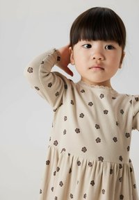 Robe beige à manches longues avec texture côtelée, présentant un motif floral en marron foncé et un col en dentelle. Jupe évasée.