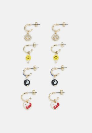 Brincos em tom de ouro com vários pendentes: círculo de strass, rosto sorridente amarelo, yin-yang e coração, com formas e texturas diversas.