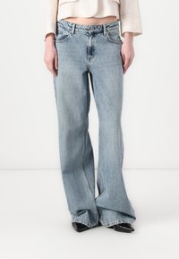 Svjetloplave traperice širokih nogavica. Imaju visoki struk, prednje džepove i suptilno izbjeljivanje. Uparene s crnim cipelama s oštrim vrhom.