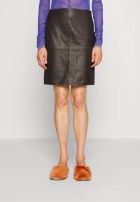 Schwarzer Leder-Bleistiftrock mit vertikalen Nähten, knielang, kombiniert mit orangefarbenen, flauschigen Hausschuhen. Glatte Textur, taillierte Passform.
