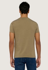 Kaki kortärmad T-shirt med rund halsringning, tillverkad av ett mjukt tyg. Matchad med denimjeans, som visar en avslappnad passform från baksidan.