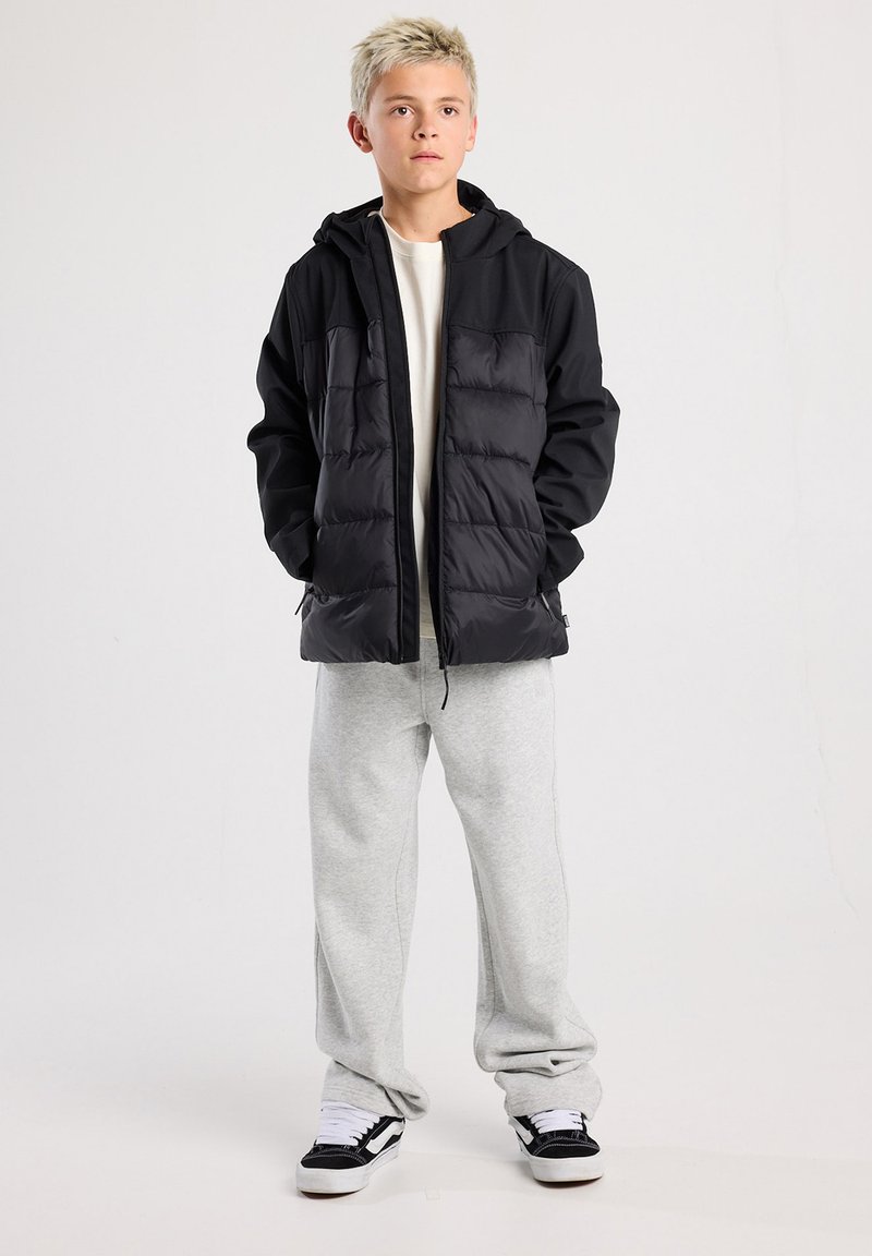 Musta pehmeä takki, jossa on vetoketju edessä, huppu ja kaksi etutaskua. Puettu kevyen paidan ja harmaiden verkkareiden päälle. Rentouttavat lenkkarit.