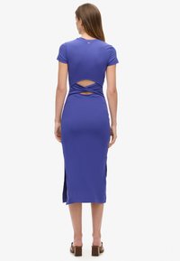 Dopasowana purpurowa sukienka midi z krótkimi rękawami, odkrytymi plecami z krzyżującym się detalem oraz bocznymi rozcięciami. Wykonana z gładkiego, elastycznego materiału.