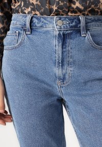 Lichtblauwe denim jeans met een hoge taille, knoopsluiting en vijf-pocket ontwerp met contrasterende stiksels. De textuur lijkt glad en stevig.