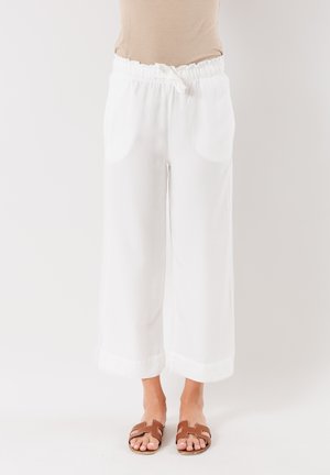 Pantaloni bianchi a gamba larga con vita regolabile, texture morbida e tasche laterali. Abbinati a sandali marroni con cinturini.