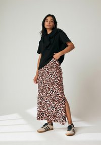 Haut noir à manches courtes avec détails volants, associé à une jupe midi à imprimé léopard. Le modèle porte des baskets beiges avec des rayures noires.