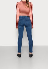 Smal jeans i blå denim med en slät yta, med hög midja, bakfickor och diskret blekning. Kombineras med en topp i röd och svart randig design.