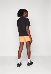 Zwarte T-shirt en oranje shorts. De T-shirt heeft een ronde hals en korte mouwen; de shorts hebben een elastische band en een rechte zoom.