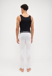 Svart tank topp og hvite leggings båret av en person, med en logo på livet. Glatt tekstur, tettsittende design. Barføtt.