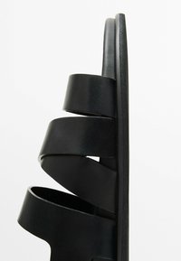 Black leather slide sandals with three wide, spiral straps. Flat sole and smooth texture with a minimalist design for easy wear.