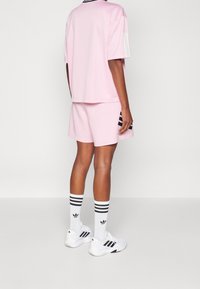 Conjunto de camiseta y pantalones cortos deportivos rosas con rayas blancas en las mangas y detalles negros. Combinado con zapatillas blancas y calcetas a rayas. Diseño minimalista.