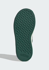 Green rubber shoe sole with a hexagonal pattern and logo. Textured for grip, featuring a slight curve at the edge. Smooth and durable material.
