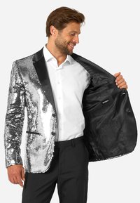 Srebrny żakiet z cekinami, z czarnymi klapami i kieszeniami, podszewką z czarnej tkaniny. Noszony na białej koszuli i czarnych spodniach, ukazujący wewnętrzne detale.